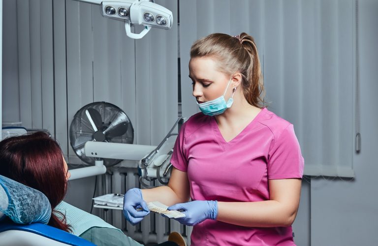 A woman dentist checks the level of teeth whitening with a dentist's color in the dentist office.